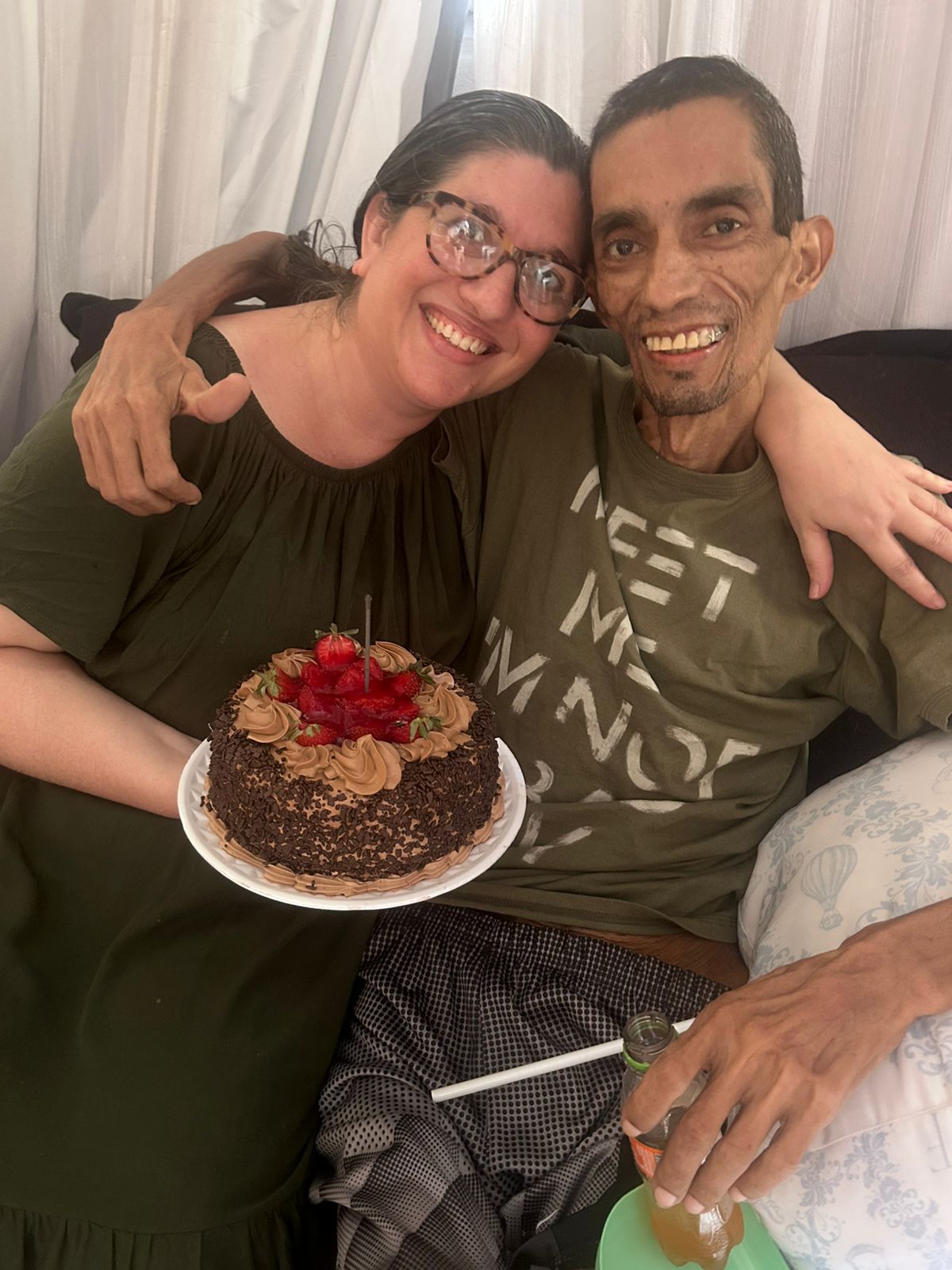 Glauco abraçado à esposa, os dois sorrindo com um bolo de aniversário.